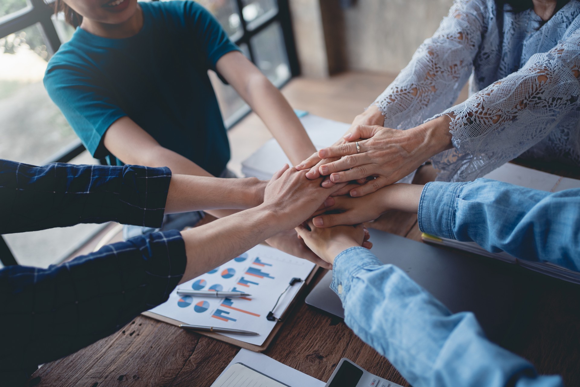 Young Asian business people shaking hands and working together as a team and having unity in working on new start-up project. Unity and Teamwork Concept.