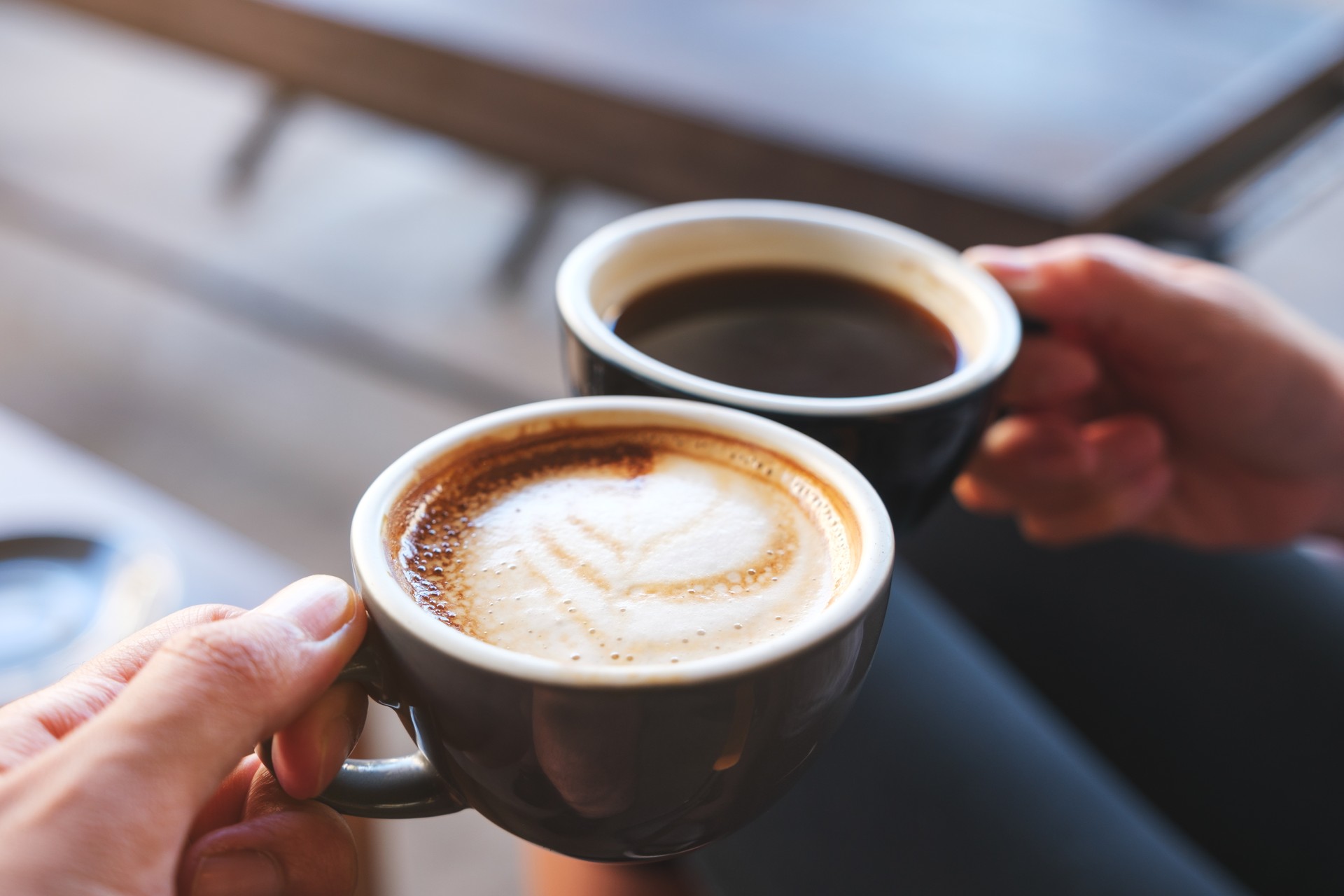 Closeup image of a man and a woman clinking white coffee mugs in cafe